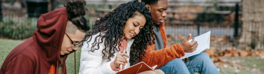 two men and a woman seated together on a grass reading their books