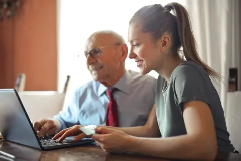 A woman and an elderly gentleman sitting down at a Laptop.