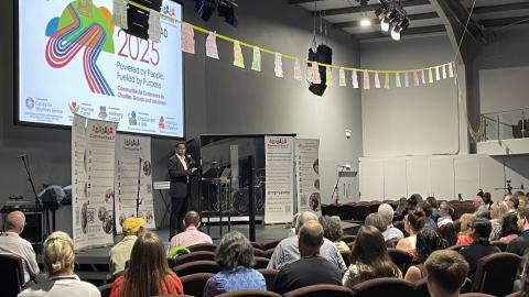 Jason John speaking from a stage to a packed auditorium