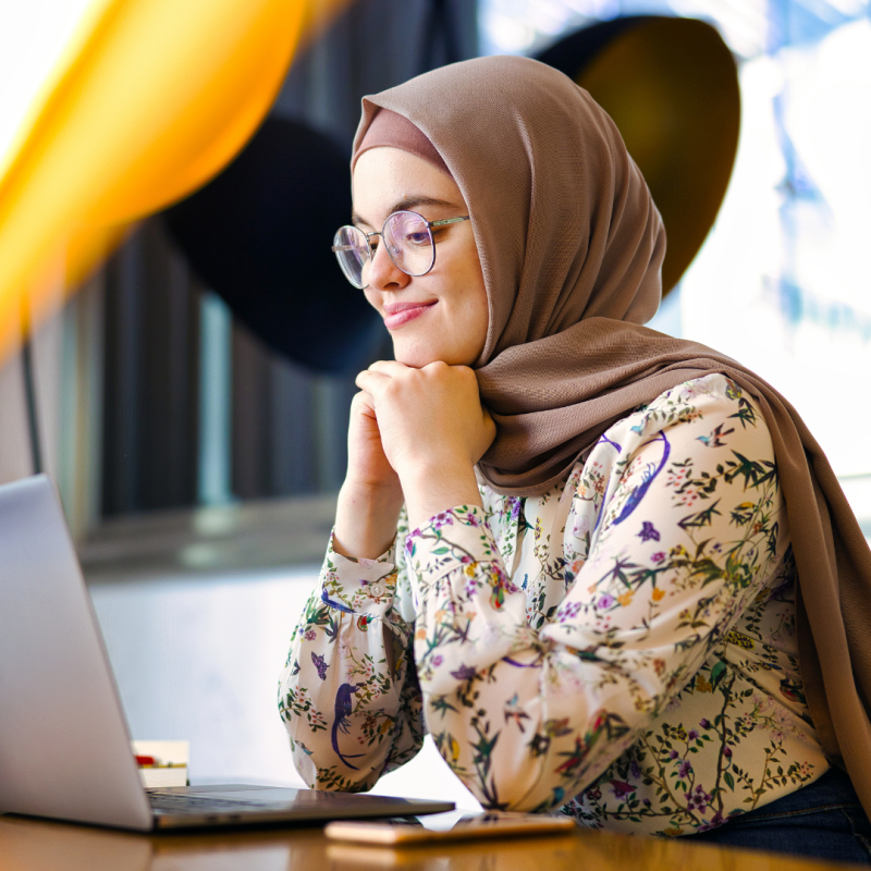 Woman wearing hijab talks to colleagues over laptop