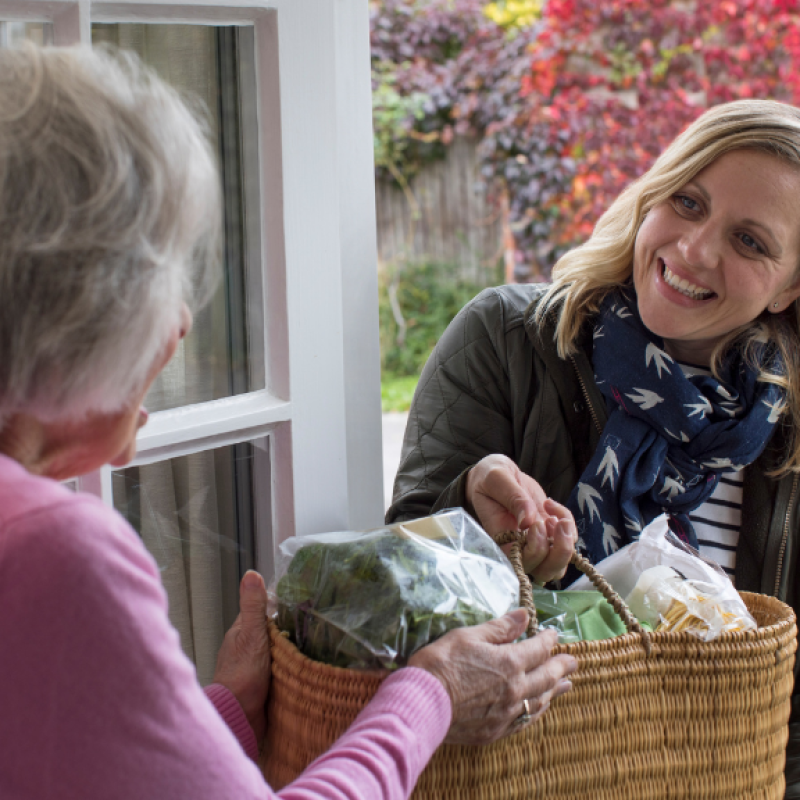 Woman helping an older lady by delivering shopping. 