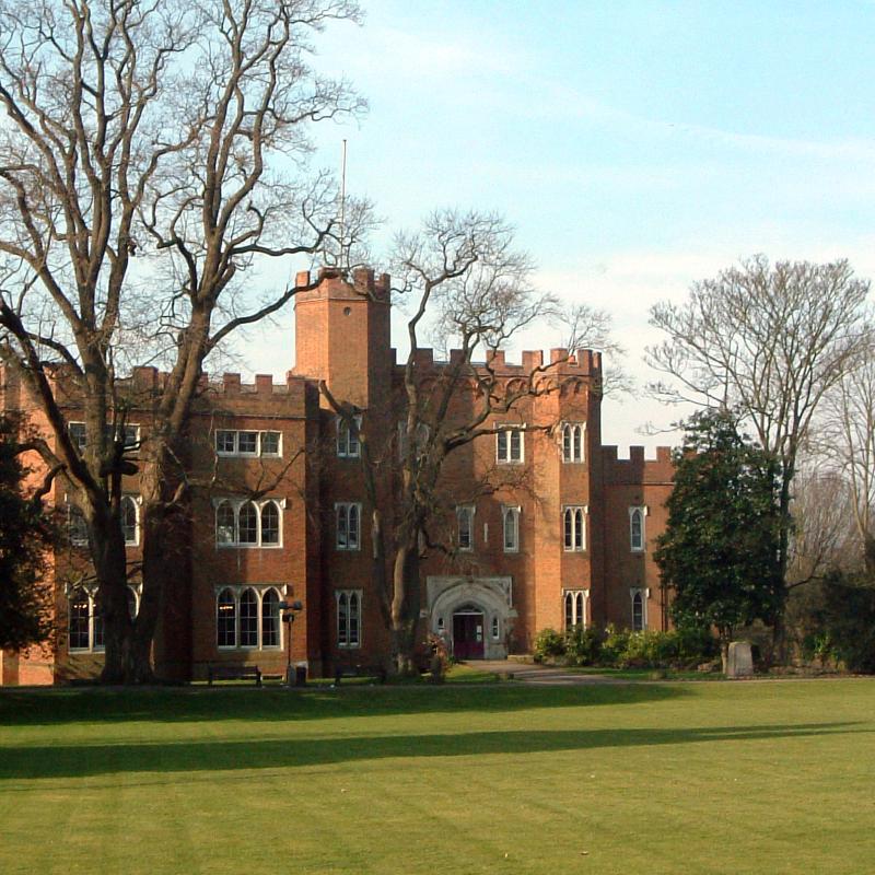 Front view of Hertford Castle from the grounds with grass and trees. 