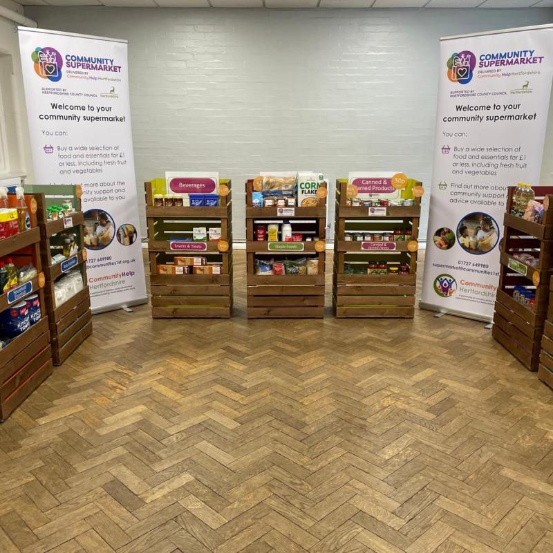 Community centre hall set up as a community supermarket with wooden stands filled with good and products around the room