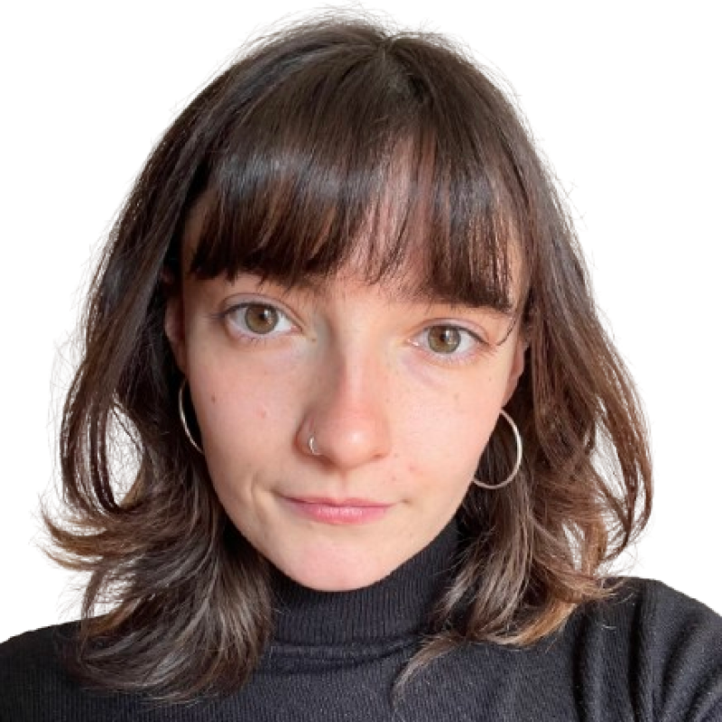 Photo of a young woman with dark shoulder length hair. She is wearing a black, high-necked top and looking at the camera