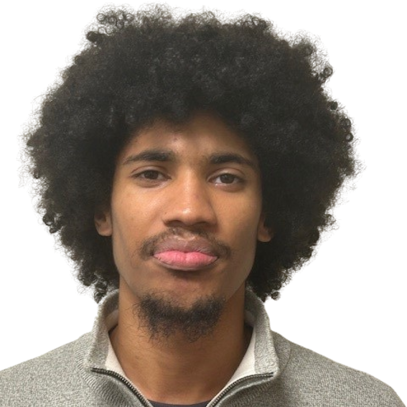 Photo of a young man with dark curly hair. He is wearing a grey collared top 
