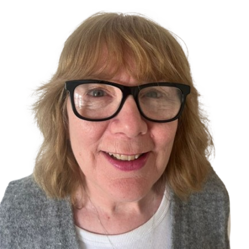 Photograph of a woman. She is wearing dark-rimmed glasses and a grey cardigan.