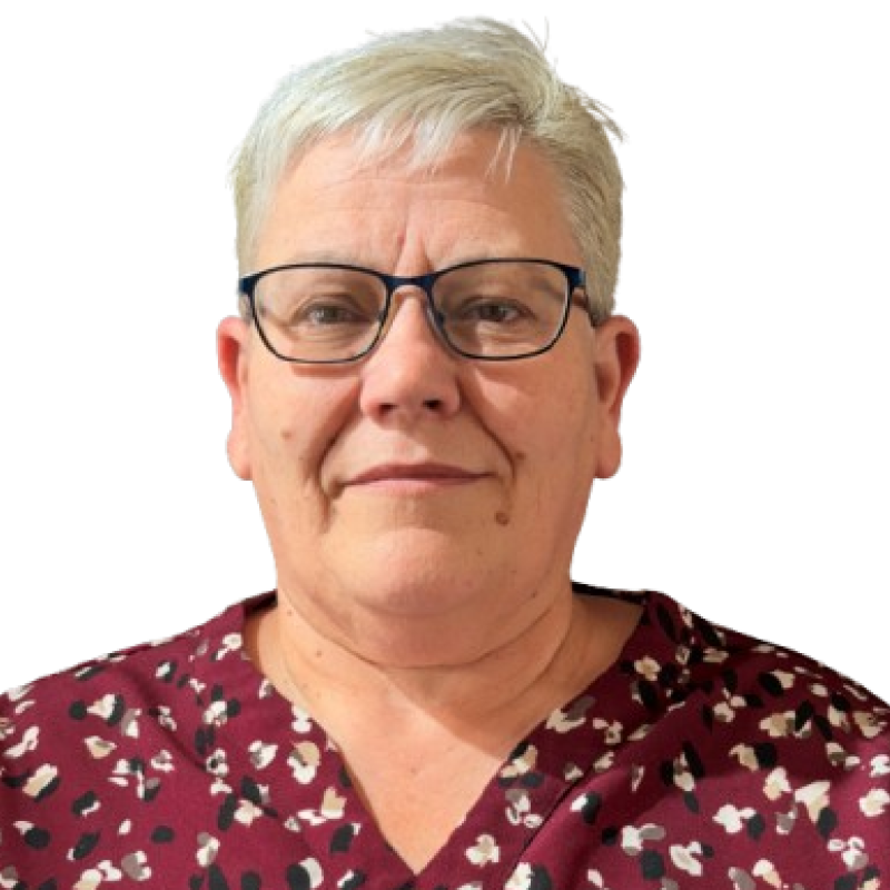 Photo of a woman. She is wearing a red dress with a pattern on it, glasses and has short cropped hair.