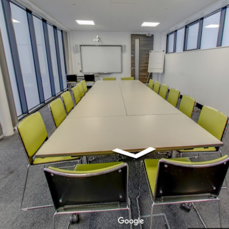 Meeting Room 1 at 96 Shenley Road. It has a long boardroom style table and green chairs around it
