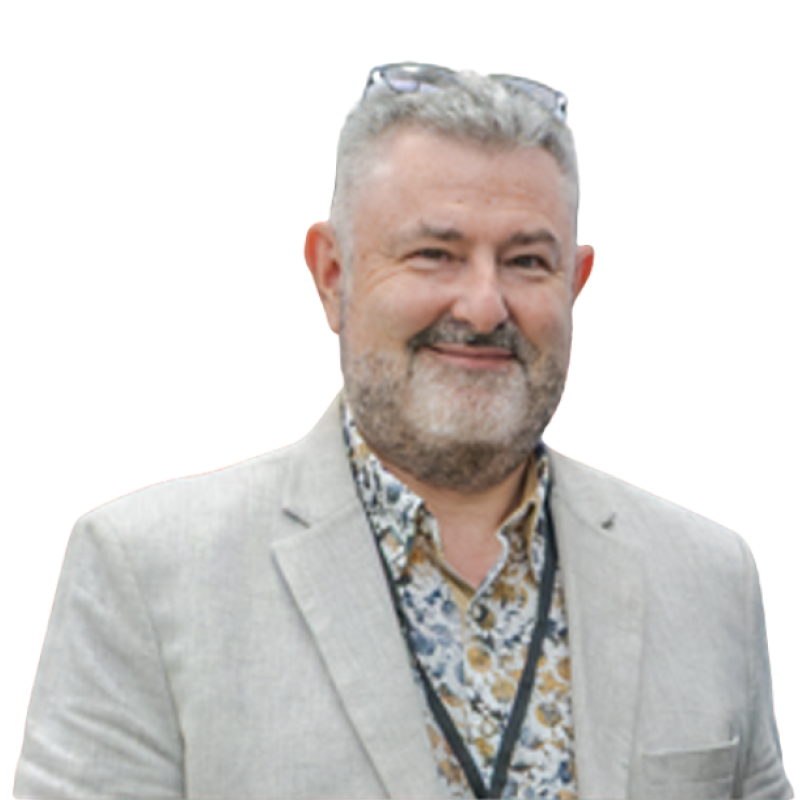Picture of a man smiling at the camera. He is wearing a light grey jacket and a floral shirt